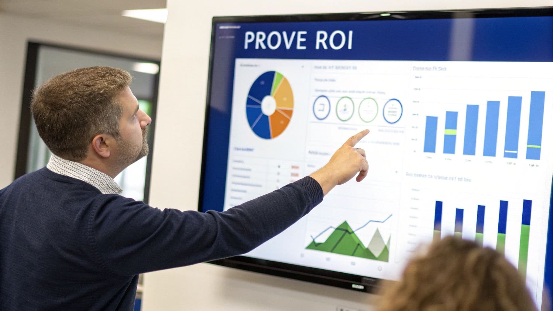 A man in a blue sweater points at a large screen displaying various data visualizations and "PROVE ROI".